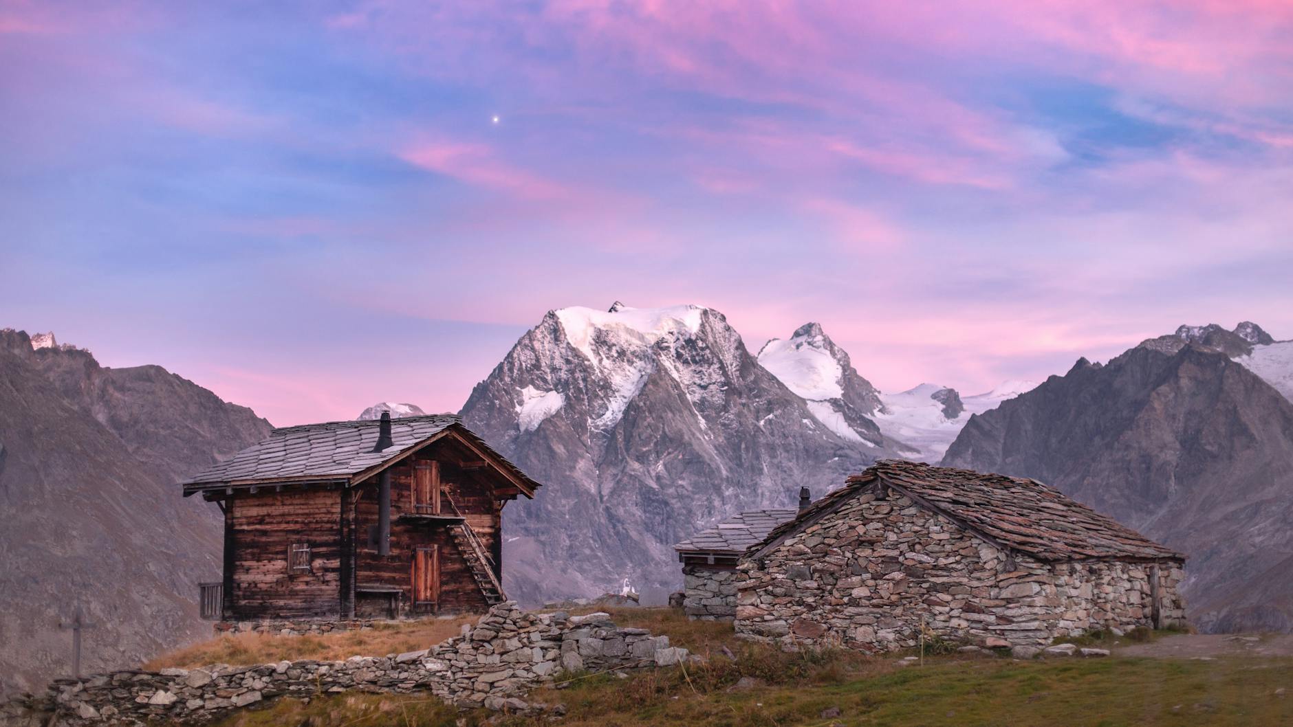 Rifugio alpino illuminato dalla luce dorata del tramonto con montagne sullo sfondo